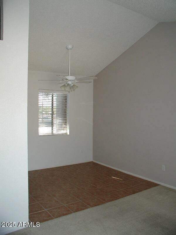 empty room with carpet floors, a ceiling fan, tile patterned floors, and vaulted ceiling