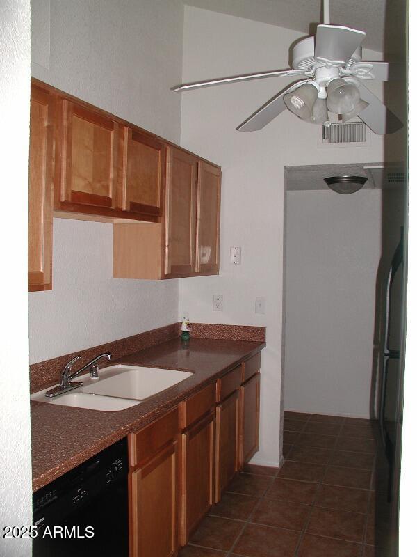 kitchen with ceiling fan, brown cabinetry, dark countertops, dishwasher, and a sink