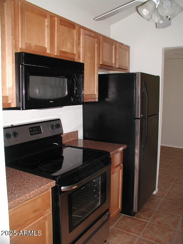 kitchen featuring stainless steel electric range oven, dark countertops, black microwave, and light tile patterned floors