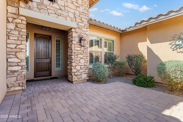 doorway to property with a tiled roof, stone siding, and stucco siding