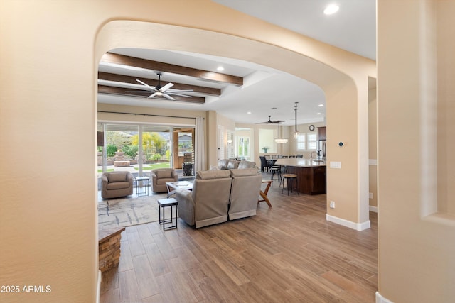 living room with beamed ceiling, arched walkways, light wood-type flooring, a ceiling fan, and recessed lighting