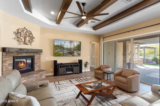 living area featuring a fireplace, beam ceiling, ceiling fan, arched walkways, and wood finished floors