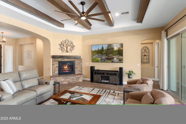 living area featuring visible vents, arched walkways, a stone fireplace, beamed ceiling, and wood finished floors