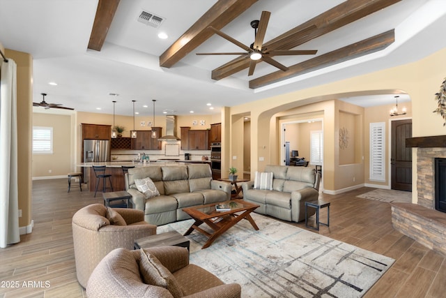 living room with ceiling fan, arched walkways, visible vents, light wood finished floors, and baseboards
