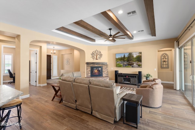 living area featuring beamed ceiling, ceiling fan, arched walkways, visible vents, and baseboards