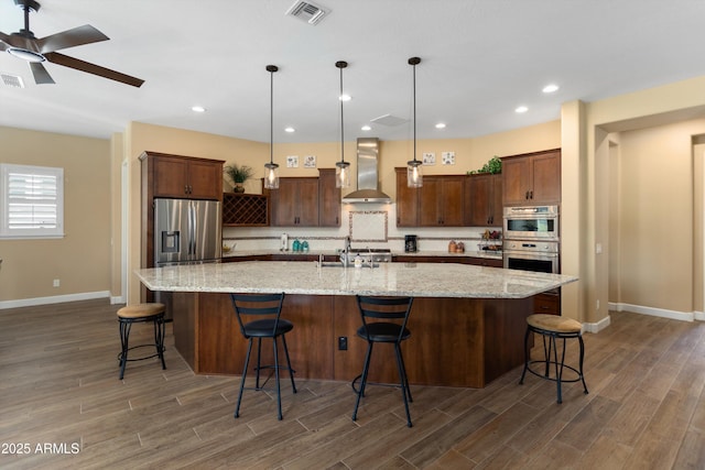 kitchen featuring baseboards, wall chimney exhaust hood, visible vents, and stainless steel appliances
