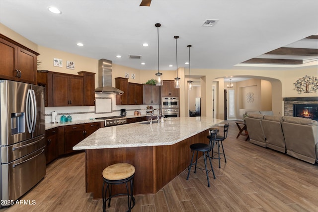 kitchen featuring arched walkways, wall chimney range hood, visible vents, appliances with stainless steel finishes, and open floor plan