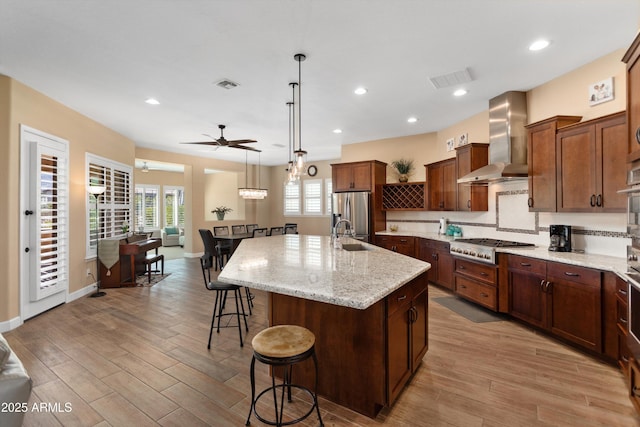 kitchen featuring a ceiling fan, visible vents, wall chimney exhaust hood, a breakfast bar area, and stainless steel appliances