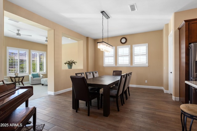 dining space featuring dark wood-style flooring, visible vents, baseboards, and ceiling fan with notable chandelier