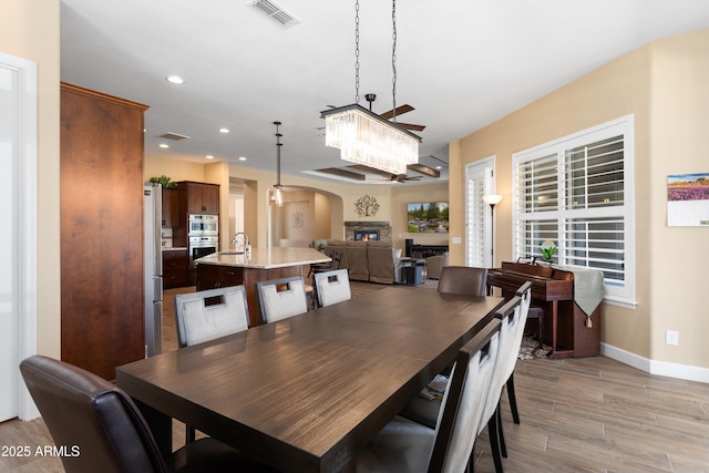 dining room featuring baseboards, an inviting chandelier, light wood-style flooring, visible vents, and arched walkways