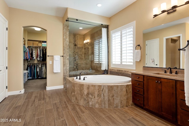 bathroom featuring a tile shower, a garden tub, vanity, wood finished floors, and a walk in closet