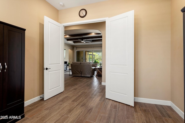 hall with baseboards, beamed ceiling, and wood finished floors