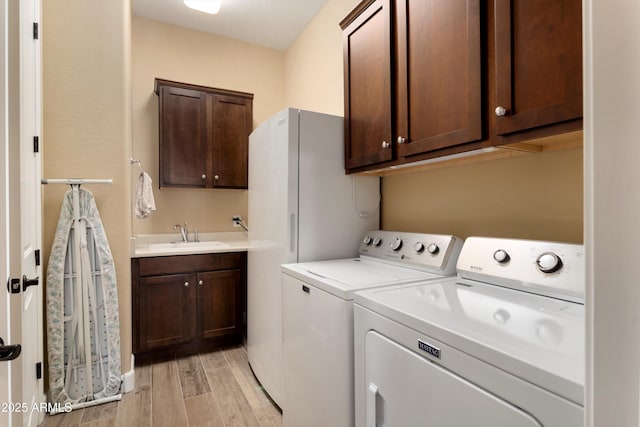 laundry room featuring light wood finished floors, a sink, cabinet space, and washer and clothes dryer