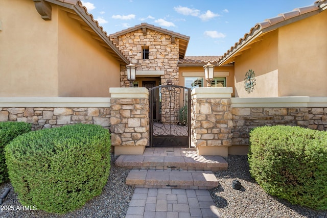 property entrance with a tiled roof, stucco siding, stone siding, and a gate