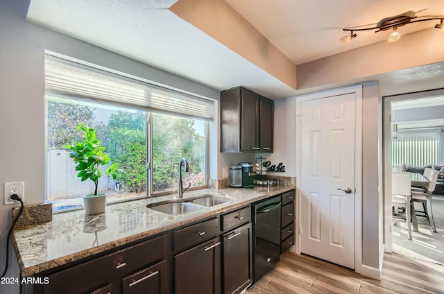 kitchen with light stone countertops, dishwasher, dark brown cabinets, and sink