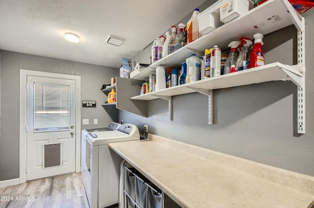 laundry area with light wood-type flooring, washing machine and dryer, and a textured ceiling