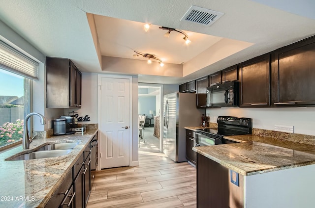 kitchen featuring black appliances, light stone counters, a tray ceiling, sink, and dark brown cabinets