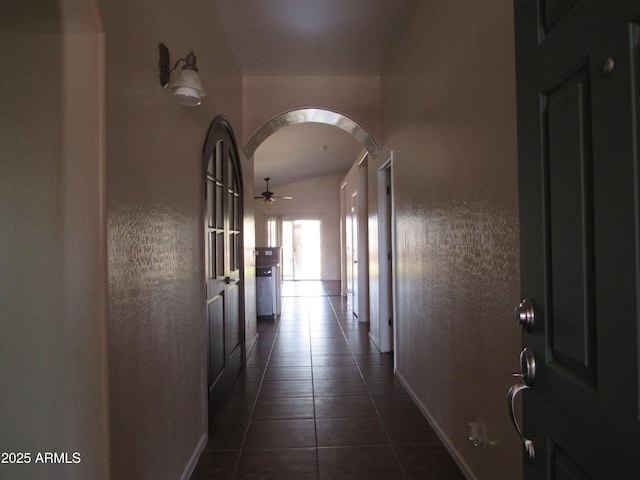 hallway featuring arched walkways, dark tile patterned flooring, and baseboards