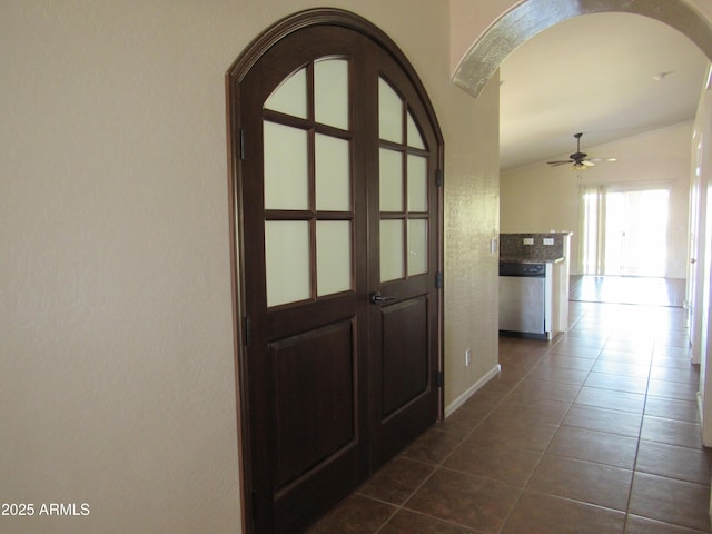 hall featuring lofted ceiling, arched walkways, and dark tile patterned flooring