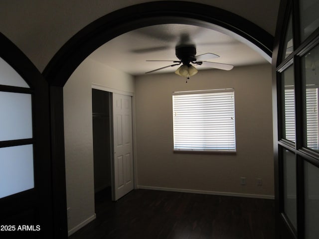 unfurnished bedroom with arched walkways, dark wood finished floors, a closet, ceiling fan, and baseboards