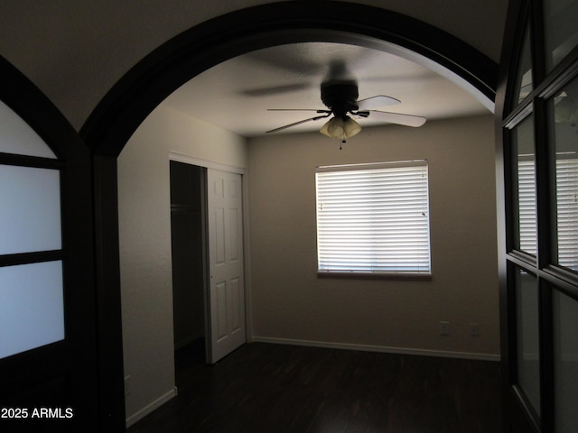 unfurnished bedroom featuring arched walkways, a ceiling fan, baseboards, a closet, and dark wood finished floors