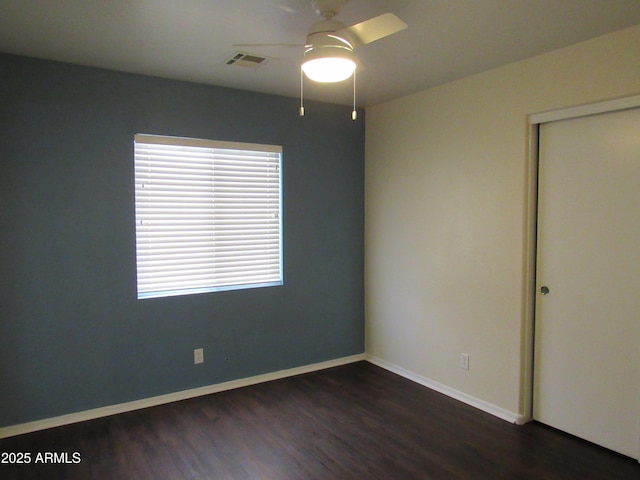 spare room featuring dark wood-type flooring, visible vents, baseboards, and a ceiling fan