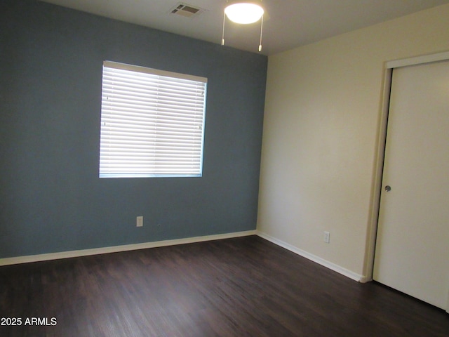 empty room with dark wood-style floors, visible vents, and baseboards