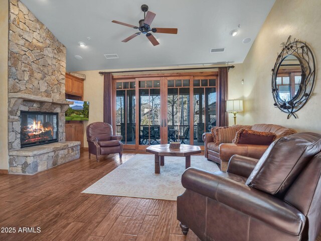 living room featuring vaulted ceiling, a stone fireplace, wood-type flooring, ceiling fan, and french doors