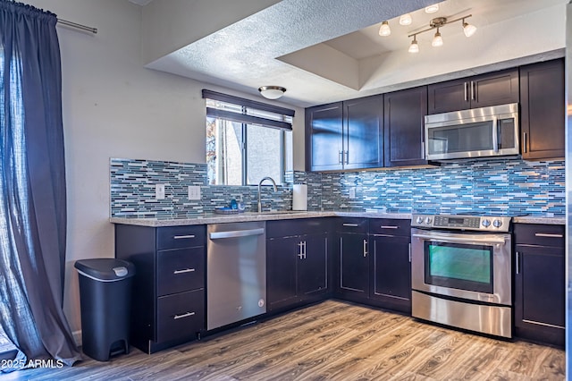 kitchen featuring sink, light hardwood / wood-style flooring, a textured ceiling, appliances with stainless steel finishes, and decorative backsplash