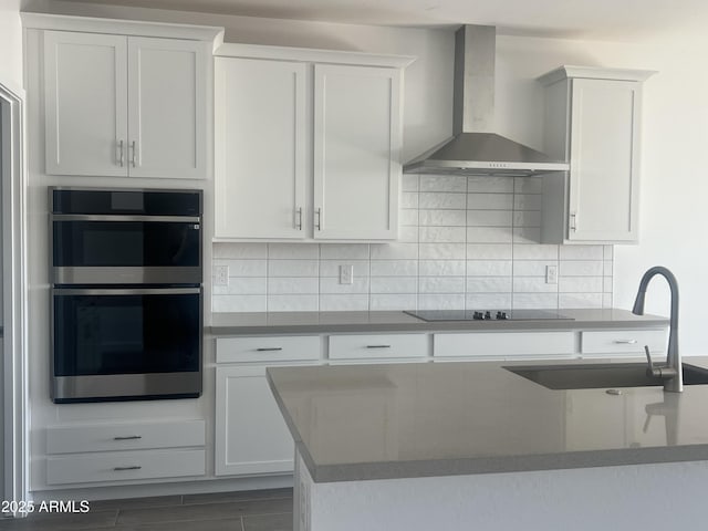 kitchen with tasteful backsplash, stainless steel double oven, white cabinetry, a sink, and wall chimney exhaust hood