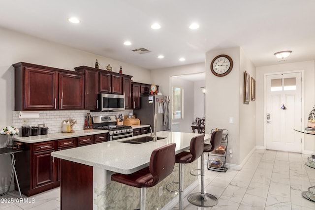 205 N 107th Dr, Avondale, AZ 85323 - kitchen featuring appliances with stainless steel finishes, light marble finish floors, dark brown cabinets, a center island with sink, and a breakfast bar area