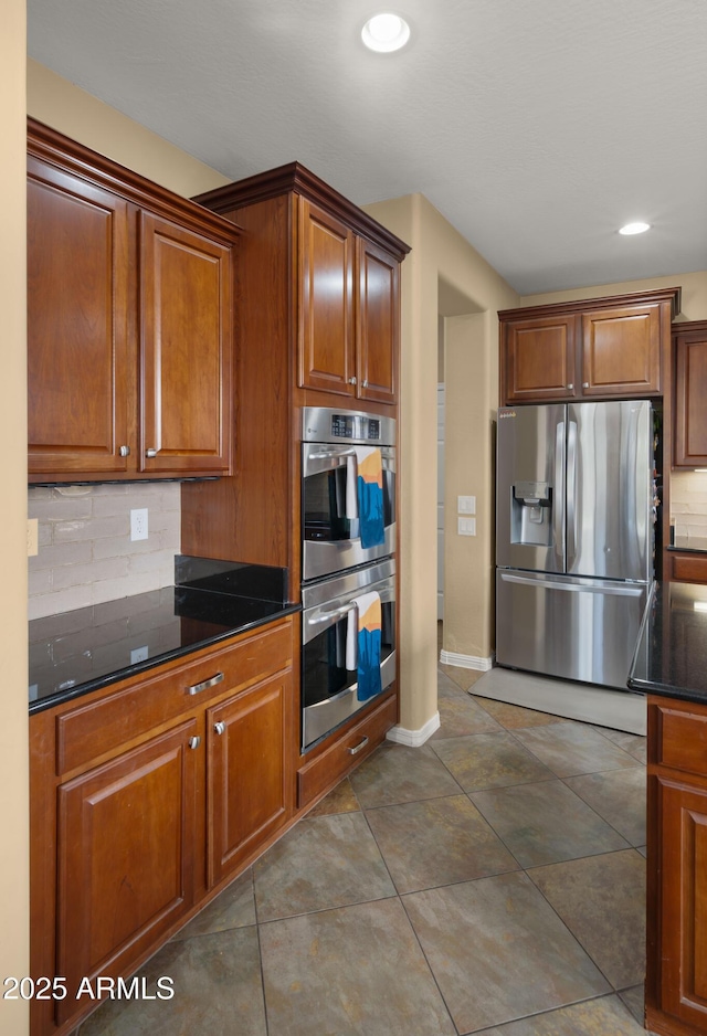 kitchen featuring baseboards, recessed lighting, dark stone countertops, backsplash, and stainless steel appliances