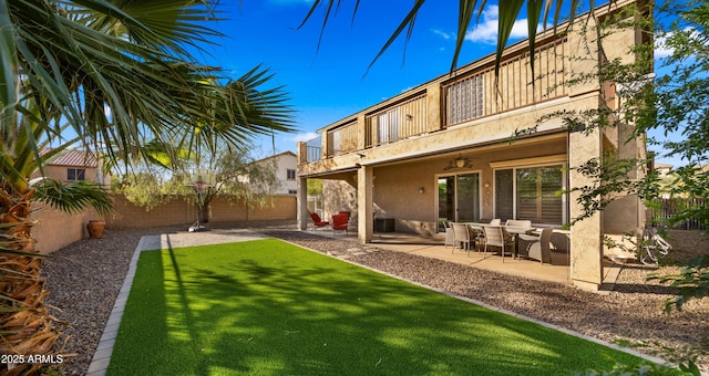 rear view of house with stucco siding, a fenced backyard, a patio area, a balcony, and a ceiling fan
