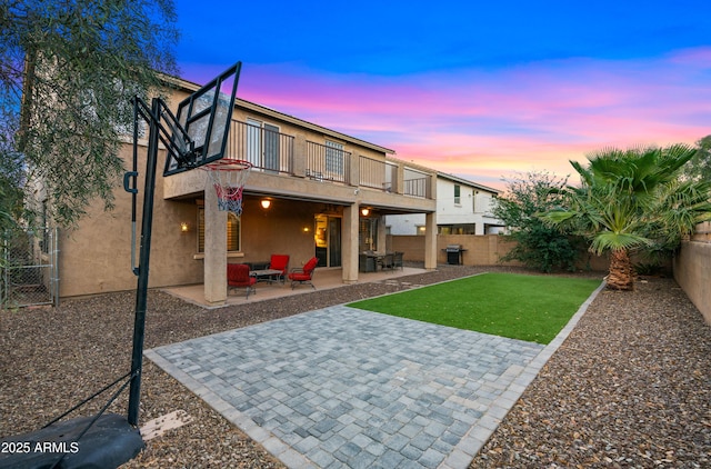 rear view of property featuring stucco siding, a fenced backyard, a balcony, a patio, and a yard
