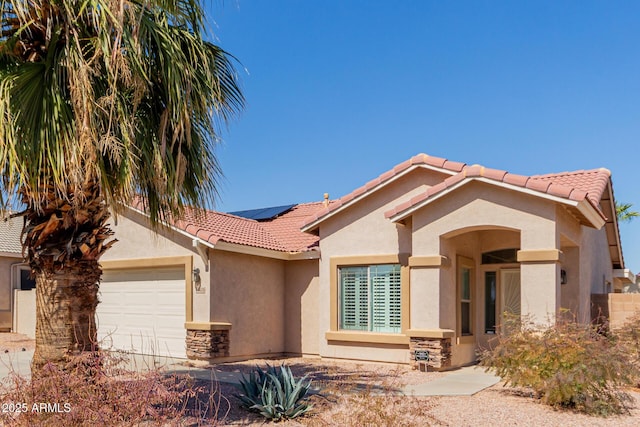 view of front facade featuring stucco siding, roof mounted solar panels, an attached garage, and a tile roof