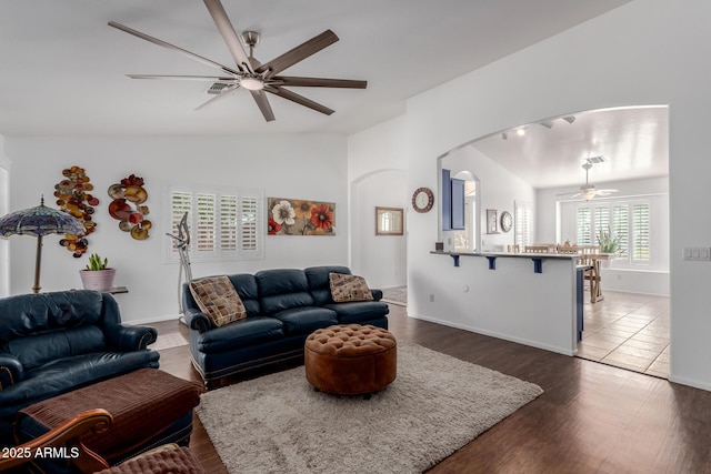 living room featuring a ceiling fan, wood finished floors, baseboards, arched walkways, and vaulted ceiling