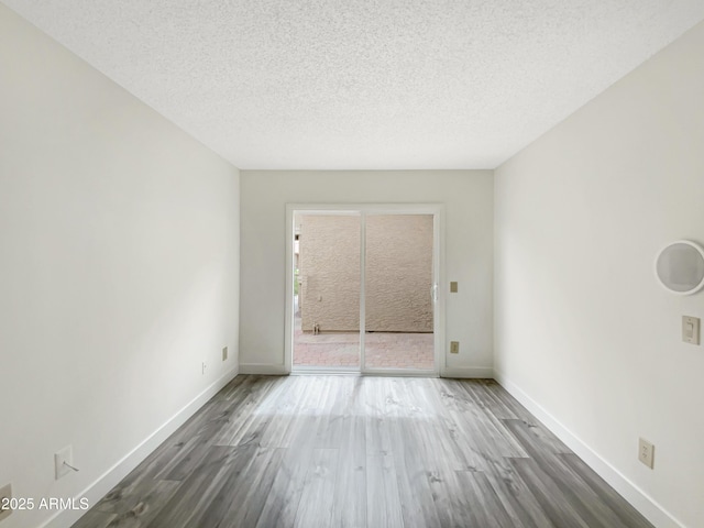 unfurnished room with a textured ceiling, baseboards, and wood finished floors