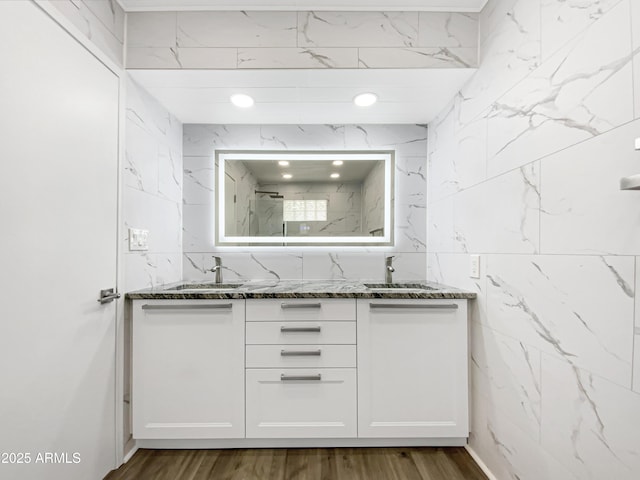 bathroom with a marble finish shower, double vanity, a sink, and wood finished floors