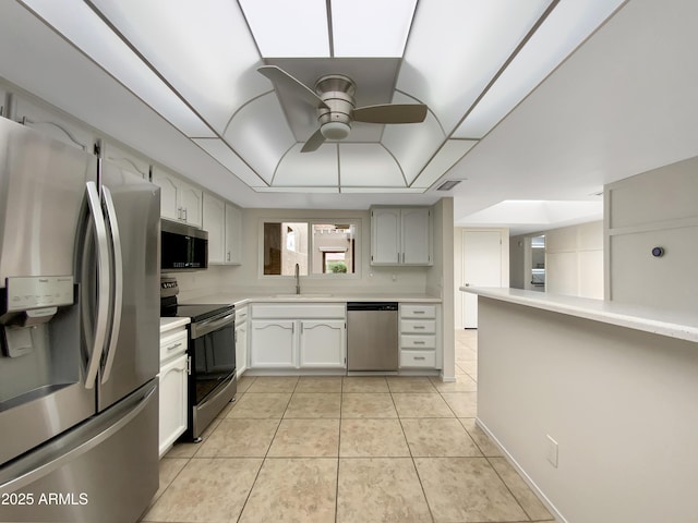 kitchen with light countertops, ceiling fan, stainless steel appliances, a sink, and a tray ceiling
