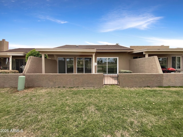 back of house featuring stucco siding, fence, and a lawn