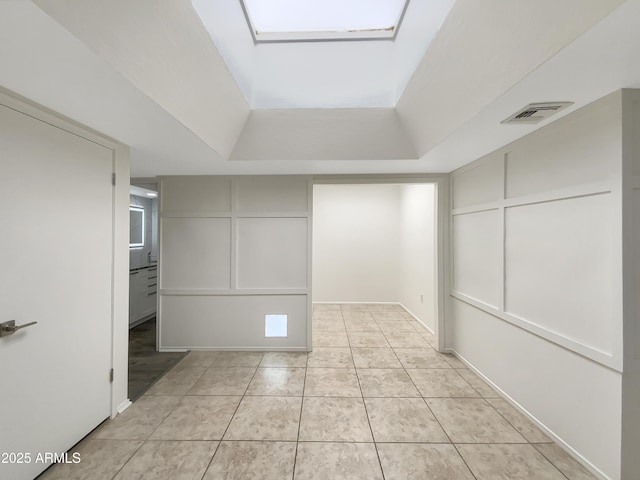 spare room with visible vents, light tile patterned floors, a decorative wall, and a raised ceiling