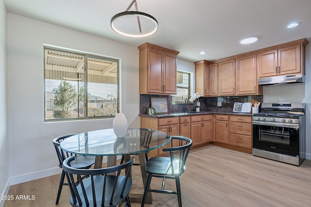 kitchen featuring sink, tasteful backsplash, hanging light fixtures, stainless steel range with gas cooktop, and light hardwood / wood-style floors