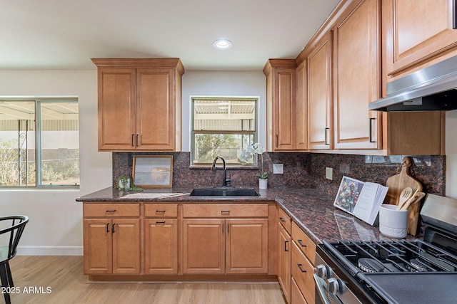 kitchen featuring stainless steel gas stove, sink, light hardwood / wood-style flooring, and dark stone counters