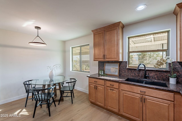 kitchen with tasteful backsplash, sink, dark stone countertops, hanging light fixtures, and light hardwood / wood-style floors