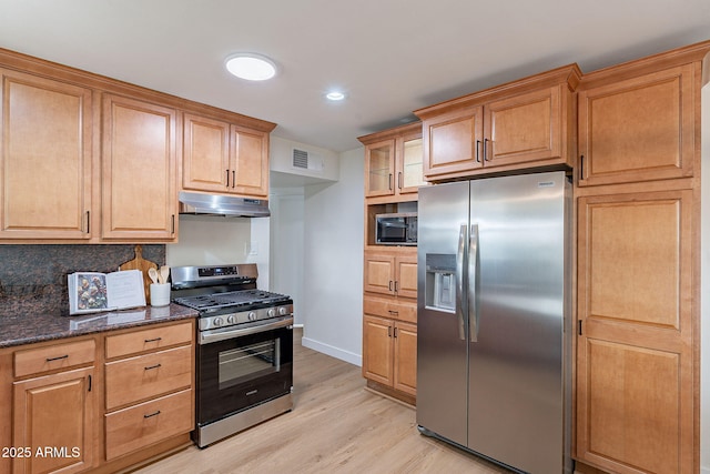 kitchen with appliances with stainless steel finishes, decorative backsplash, light wood-type flooring, and dark stone counters