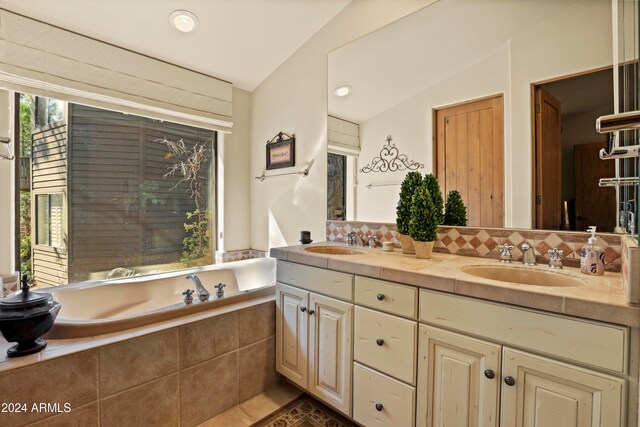 bathroom with tasteful backsplash, tile patterned flooring, tiled tub, vaulted ceiling, and vanity