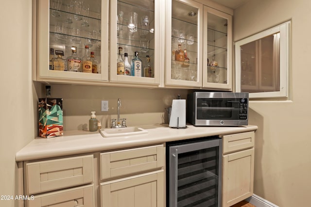 bar featuring cream cabinets, beverage cooler, and sink