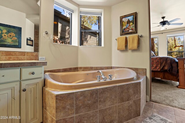 bathroom with tile patterned flooring, ceiling fan, vanity, and tiled tub