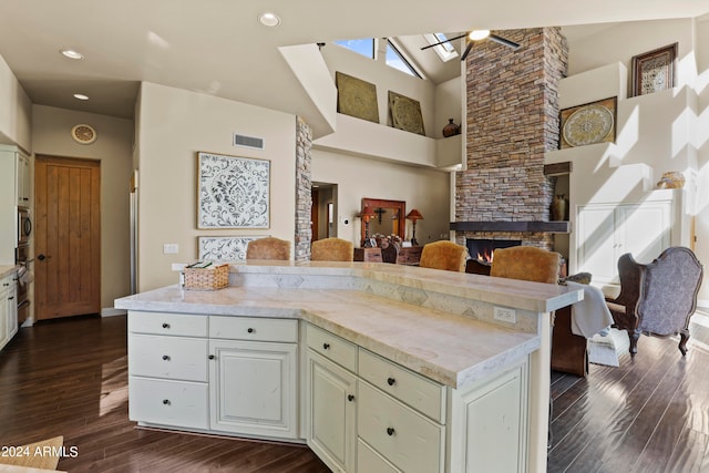 kitchen featuring dark wood-type flooring, oven, a stone fireplace, ceiling fan, and beamed ceiling