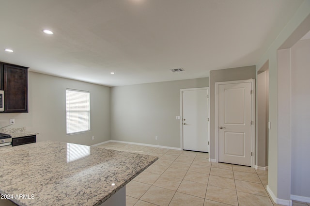 kitchen featuring light tile patterned floors, light stone counters, white microwave, visible vents, and dark brown cabinets